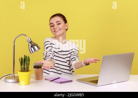 Une femme souriante et positive, responsable de bureau en chemise rayée, saluant avec joie un nouvel employé levant les bras pour hug, une femme généreuse faisant un don. Studio d'intérieur tourné isolé sur fond jaune. Banque D'Images