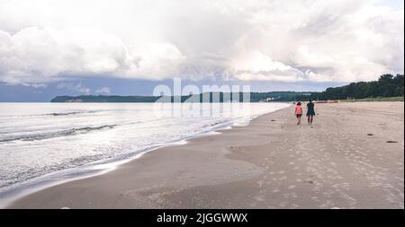 Deux femmes marchent le long d'une plage de mer vide. Banque D'Images