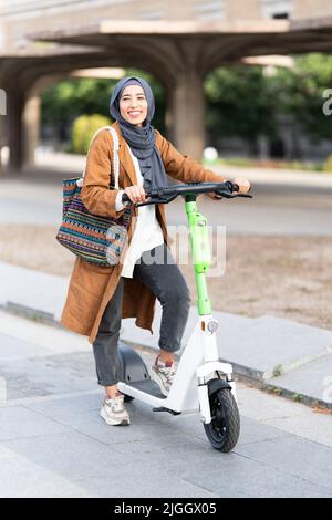 Femme musulmane utilisant un scooter électrique dans la rue Banque D'Images
