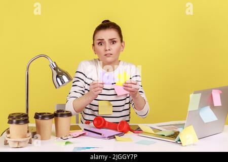 Portrait d'une femme confuse recouvert de notes adhésives contenant des pièces de puzzle colorées, deux parties d'une, symbole de connexion et d'Union. Studio d'intérieur tourné isolé sur fond jaune. Banque D'Images