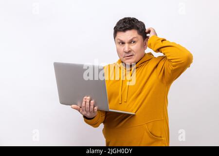 Portrait pensive homme pensif avec tenir un ordinateur portable et la tête de frottement regardant loin, pensant à nouveau projet d'entreprise, portant le style urbain de sweat à capuche. Studio d'intérieur isolé sur fond blanc. Banque D'Images