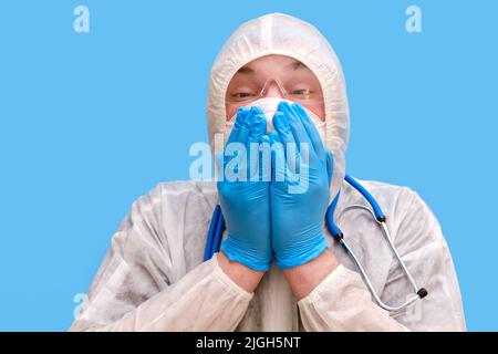 Homme médecin medic dans un uniforme de costume de protection avec des lunettes et un masque facial sur un fond bleu studio.Paramédic en vêtements de protection antiviral blancs Banque D'Images