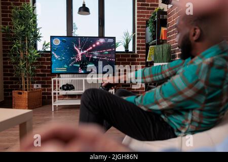 Homme gai utilisant le joystick et la console pour jouer à des jeux vidéo à la maison se réunissant avec des amis, boire de la bière et manger des collations. Groupe de personnes s'amusant avec la compétition de jeu, le divertissement. Banque D'Images