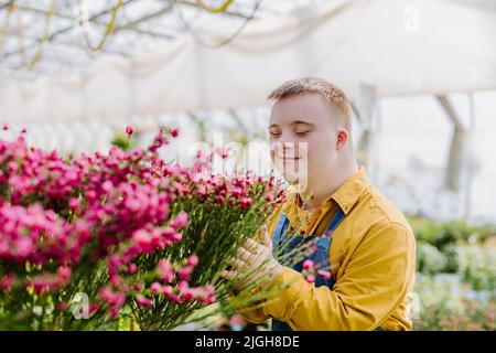 Jeune employé heureux avec le syndrome de Down travaillant dans le centre de jardin, prenant soin des fleurs. Banque D'Images