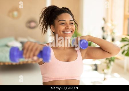 Entraînement avec poids. Bonne femme afro-américaine faisant des exercices avec des haltères, renforçant son corps à la maison Banque D'Images