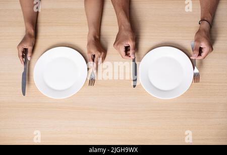 Les mains d'une femme et d'un homme afro-américain millénaire affamés tiennent les couverts près des assiettes vides sur la table Banque D'Images