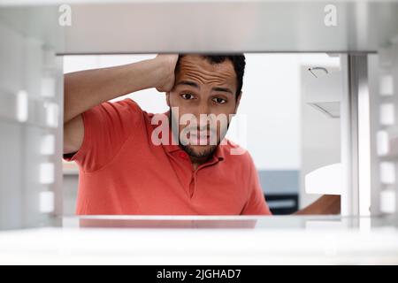 Faim affamée choqué déçu jeune africain américain vérifie que le frigo vide a du stress dans la cuisine Banque D'Images