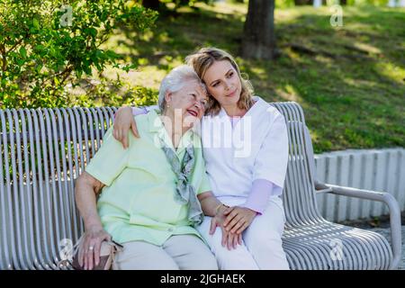 Soignant avec une femme âgée assise sur le banc dans le parc en été, embrassant. Banque D'Images