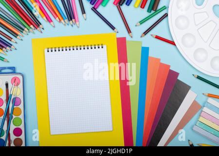 Feuille de papier vierge de cahier de mathématiques, fournitures scolaires d'art pour la peinture, sur fond bleu avec espace de copie pour le texte. Crayons colorés, marqueurs Banque D'Images