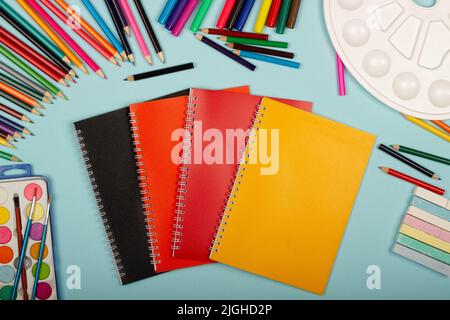 Carnets multicolores, noir, rouge et orange, fournitures scolaires d'art pour la peinture, sur fond bleu avec espace de copie pour le texte. Crayons colorés, marque Banque D'Images