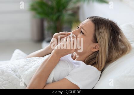 Femme malade couché au lit, éternuant nez Banque D'Images