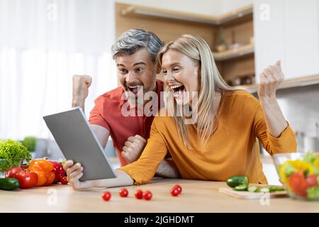 Homme et femme émotionnels utilisant une tablette numérique pendant la cuisson Banque D'Images