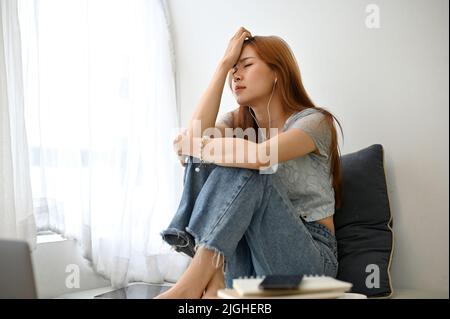 Une jeune femme asiatique frustrée assise dans son salon, pensant à ses problèmes de vie, dépression, pleurer et se sentir déçue. Banque D'Images