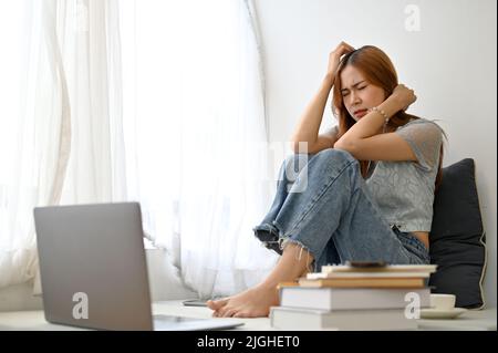 Stressé frustrée jeune asiatique assis dans son salon à la maison, pensant à ses problèmes de vie, la dépression, pleurer et se sentir déçu. Banque D'Images