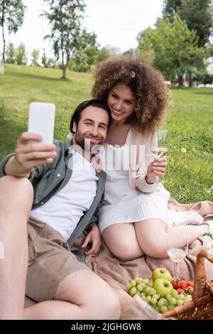 jeune couple joyeux prenant le selfie sur un smartphone pendant le pique-nique d'été dans le parc Banque D'Images
