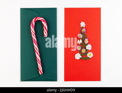 Arbre de Noël fait de fleurs séchées pressées sur une carte postale rouge. Sur l'enveloppe verte se trouve une canne à sucre. Carte de vœux de Noël faite à la main en oshibana Banque D'Images