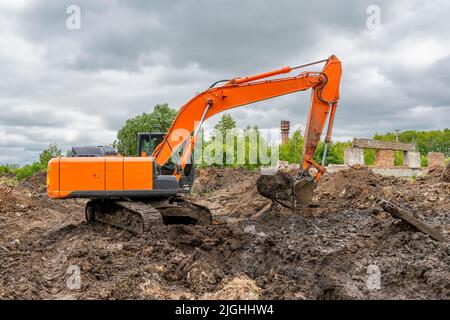 Une grande pelle sur chenilles orange creuse (creusant une tranchée) sur fond d'arbres verts et d'un spectaculaire ciel d'été. Banque D'Images