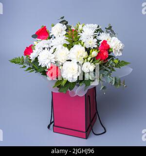 Magnifique bouquet dans une boîte cadeau rose est sur fond bleu. Bouquet de fleurs aux roses roses, pivoines blanches, chrysanthèmes et branches Banque D'Images