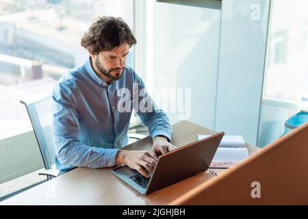 Au-dessus de la vue d'un homme d'affaires mûr concentré en tenue formelle travaillant sur un ordinateur portable dans un bureau contemporain Banque D'Images