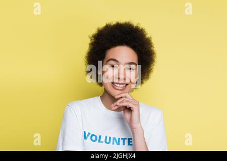 heureux volontaire afro-américain touchant le menton et souriant à la caméra isolée sur jaune Banque D'Images