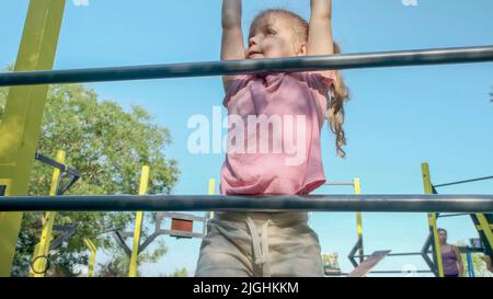 Une petite fille monte l'échelle de gymnastique sur un terrain de sport ouvert à l'extérieur. Une petite fille mignonne à ramper sur une échelle de sport verticale dans le parc de la ville le jour du soleil. Banque D'Images