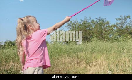 Une petite fille joue avec un filet de papillon de grande herbe dans le parc de la ville. Une petite fille mignonne joue avec un filet d'insecte aérien dans un pré le jour du soleil. Banque D'Images