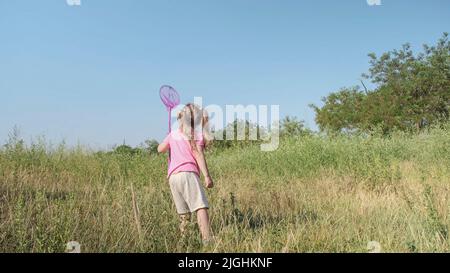 Une petite fille joue avec un filet de papillon de grande herbe dans le parc de la ville. Une petite fille mignonne joue avec un filet d'insecte aérien dans un pré le jour du soleil. Banque D'Images