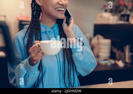 Tasse de café à la main d'une femme barman ou barista, parlant au téléphone portable et souriant. Banque D'Images