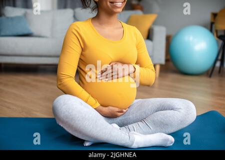 Soins du corps et entraînement. Souriante jeune femme enceinte noire touche le gros ventre, sent le mouvement de bébé Banque D'Images