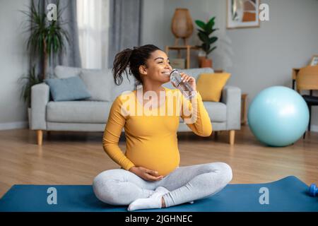 Joyeuse jolie femme afro-américaine enceinte millénaire pratique le yoga et boit l'eau de la bouteille Banque D'Images