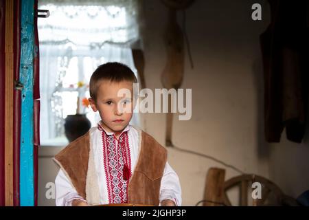 Petit garçon slave biélorusse ou ukrainien dans des vêtements nationaux sur un fond rustique. Banque D'Images