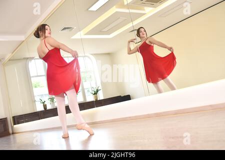 une jeune ballerine en robe rouge et des chaussures pointe effectuent des exercices dans un studio de danse Banque D'Images