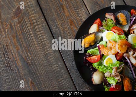 Assiette à salade de fruits de mer sur demi-espace en bois. Portion de salade avec crevettes grillées, moules et pieuvre sur le côté de la photo sur fond de bois W Banque D'Images