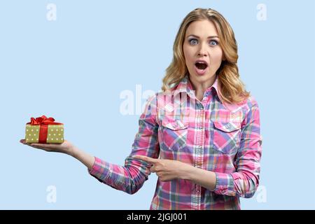 Une jeune femme caucasienne choquée se réjouit de son cadeau d'anniversaire. Femme surprise tenant une boîte cadeau sur fond de couleur. Banque D'Images