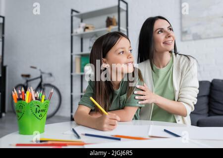 baby-sitter rêveuse et fille heureuse avec crayon coloré regardant loin Banque D'Images