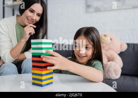 baby-sitter positif jouant en bois tour jeu avec enfant heureux dans la salle de séjour Banque D'Images