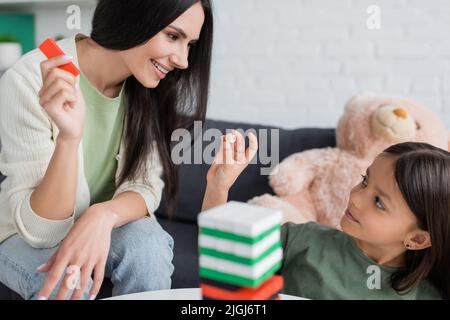 joyeux baby-sitter jouant des blocs de bois jeu avec fille dans le salon Banque D'Images