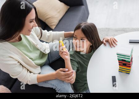 vue de dessus de la bonne baby-sitter jouant en bois tour jeu avec fille positive dans le salon Banque D'Images