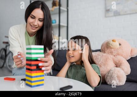 bonne baby-sitter jouer à des blocs de bois jeu avec fille souriante dans le salon Banque D'Images