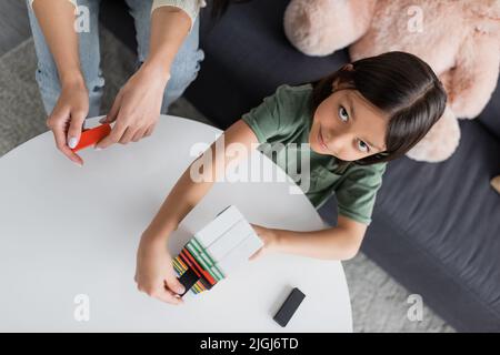 vue de dessus de babysitter jouer à des blocs de bois jeu avec la fille heureuse dans le salon Banque D'Images