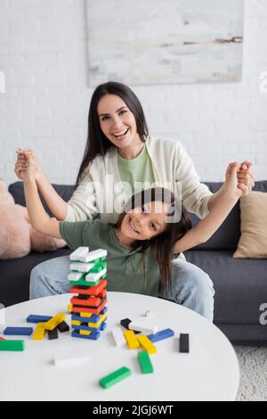 joyeux baby-sitter jouant au jeu de tour en bois avec une fille joyeuse dans le salon Banque D'Images