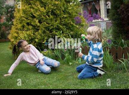 garçon et fille de 6-7 ans jouent avec des bulles assis dans le parc sur l'herbe. le concept d'une enfance heureuse, relations amicales entre les enfants, Banque D'Images