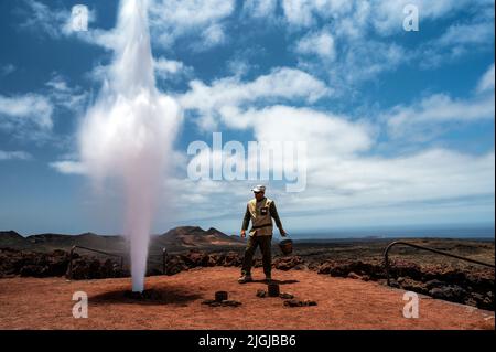Un travailleur montre aux visiteurs un grand jet de vapeur d'eau produit en versant de l'eau dans un conduit dans le sol sous une zone volcanique à haute température dans Banque D'Images