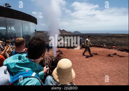 Un travailleur montre aux visiteurs un grand jet de vapeur d'eau produit en versant de l'eau dans un conduit dans le sol sous une zone volcanique à haute température dans Banque D'Images
