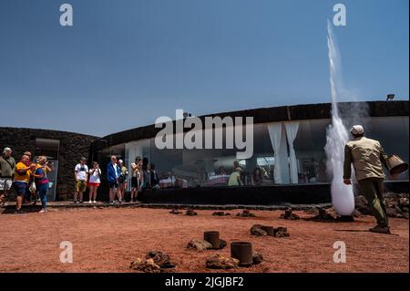 Un travailleur montre aux visiteurs un grand jet de vapeur d'eau produit en versant de l'eau dans un conduit dans le sol sous une zone volcanique à haute température dans Banque D'Images
