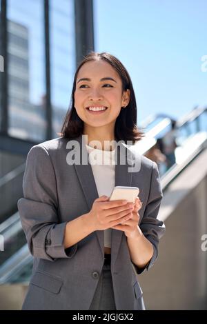 Jeune femme d'affaires asiatique gaie debout dans la rue urbaine à l'aide du téléphone. Banque D'Images