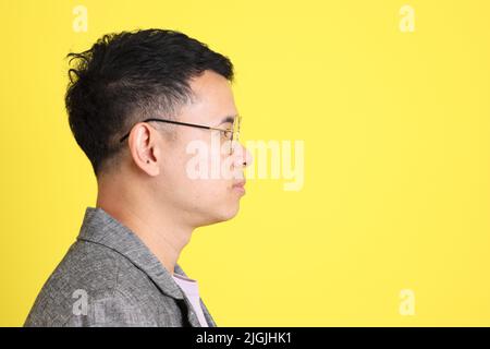 L'homme LGBTQ asiatique avec blazer gris debout sur fond jaune. Banque D'Images