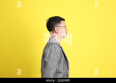 L'homme LGBTQ asiatique avec blazer gris debout sur fond jaune. Banque D'Images