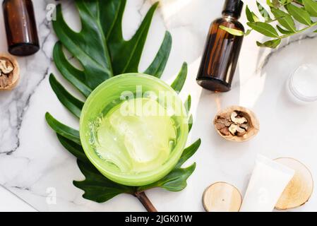 Une belle composition avec de l'huile, de l'aloès, du savon et des noix. Bouteilles avec produits cosmétiques spa sur fond de palmier, vue du dessus. Procédures du salon de beauté Banque D'Images