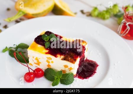 Gros plan du cheesecake avec de la cerise et de la confiture sur une assiette blanche. Dessert sucré, potiron et hop sur un premier plan flou. Menu d'automne, cuisine du restaurant Banque D'Images